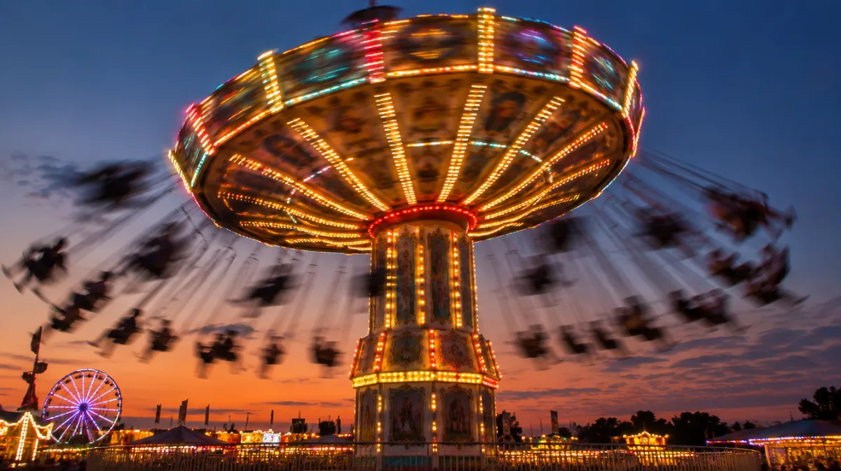A spinning fairground swing ride photographed with motion blur at dusk