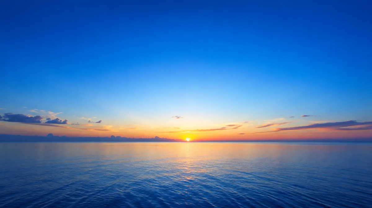 A wide clear sky, deep blue overhead and pale near the horizon, over a calm sea